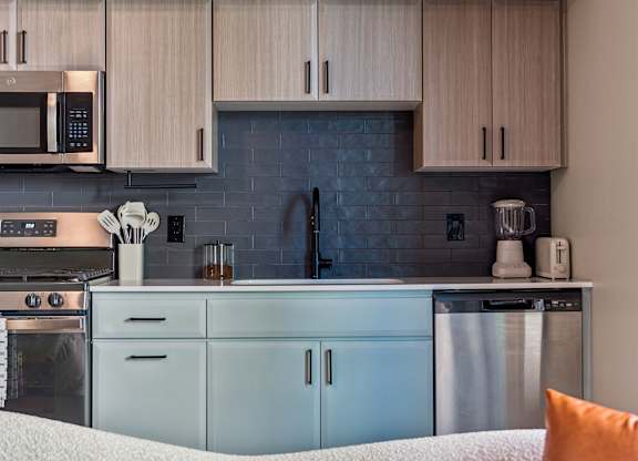 A modern kitchen with a white couch and a blue backsplash.