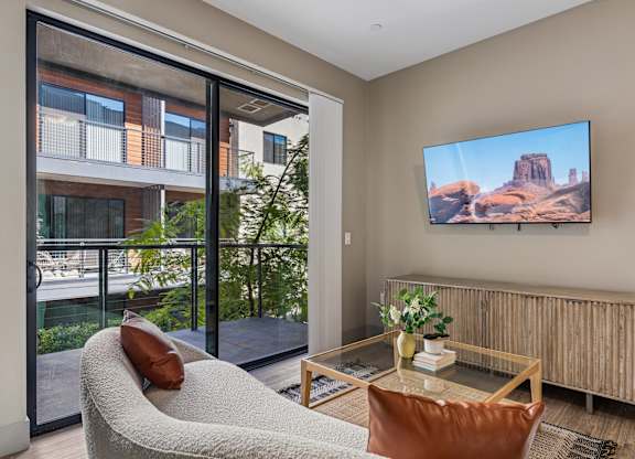 A living room with a couch, a table, a chair, and a television displaying a desert landscape.