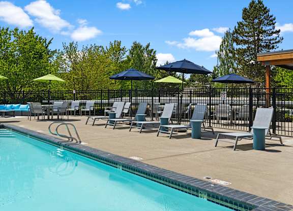 A pool with a blue umbrella and chairs.