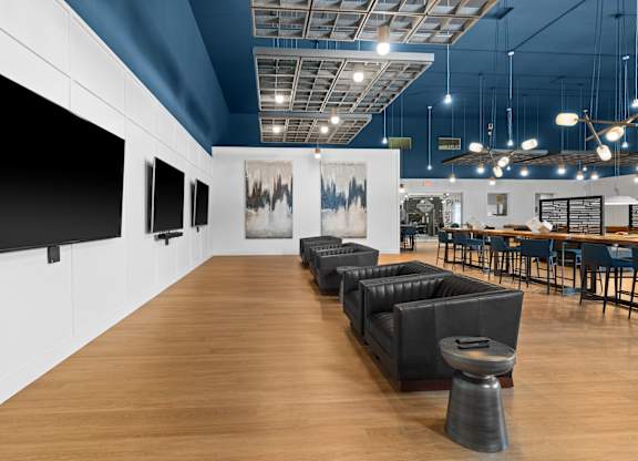 A room with a long wooden floor and a row of black sofas.