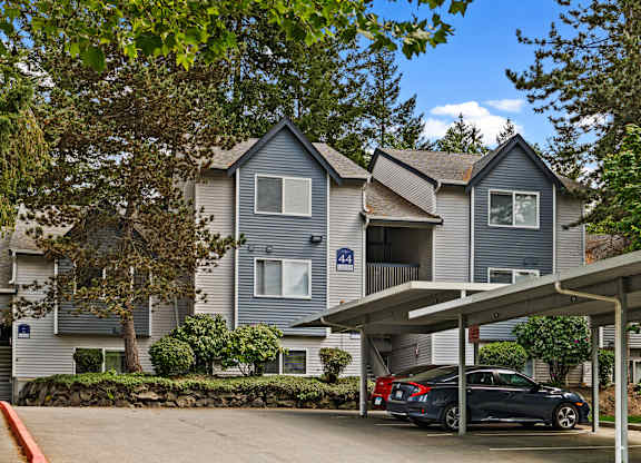 A car is parked under a covered area in front of a two-story building with a blue and white sign on the front.