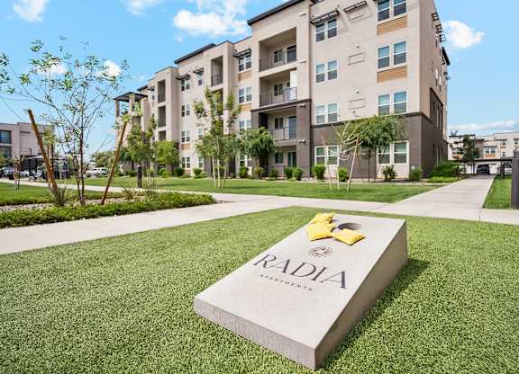A large stone block with the word RADIA on it sits in the grass in front of apartment buildings.