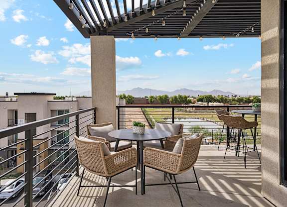 A patio with a table and chairs overlooking a parking lot and buildings.