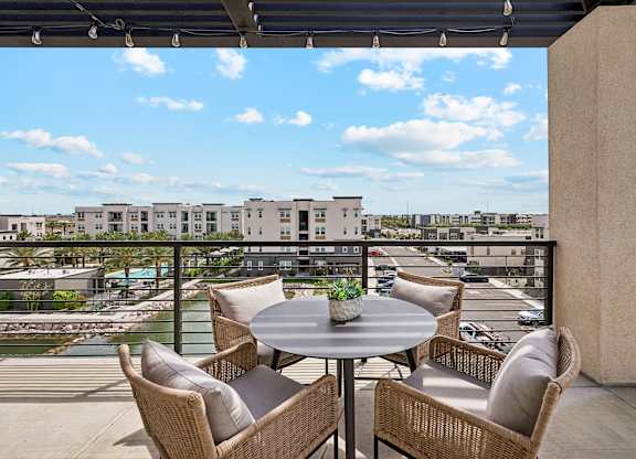 A patio with a table and chairs overlooking a pool and buildings.
