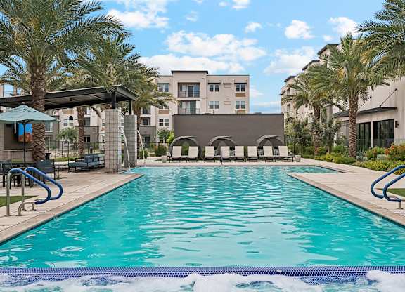 A large swimming pool in front of a building with palm trees.