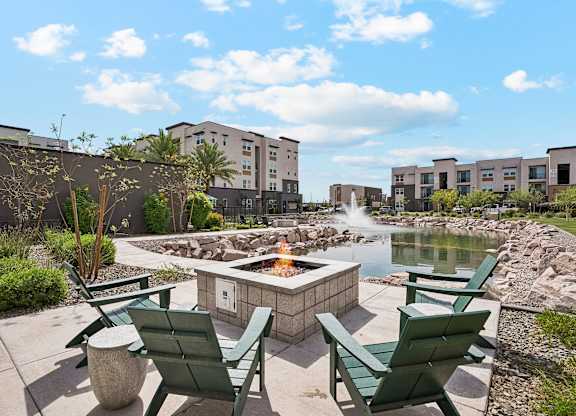 A fire pit in the middle of a patio surrounded by green chairs.