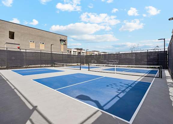 A tennis court with blue and white markings is surrounded by a fence and a building.