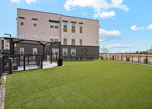 A large grassy area in front of a building with a fence and a small shelter.