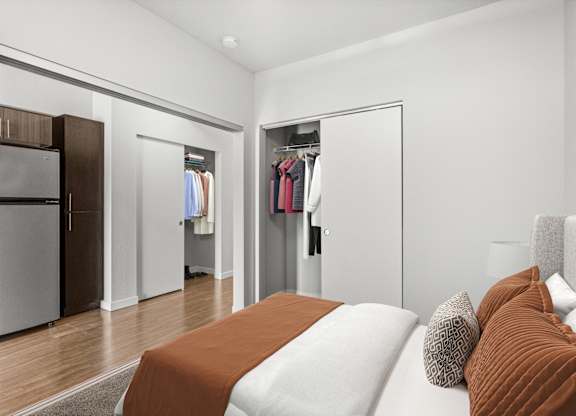 A bedroom with a bed, pillows, and a closet with clothes hanging.