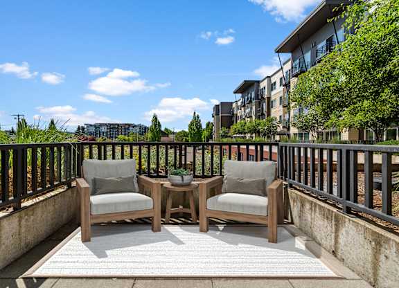 A balcony with two chairs and a table is set up on a sunny day.