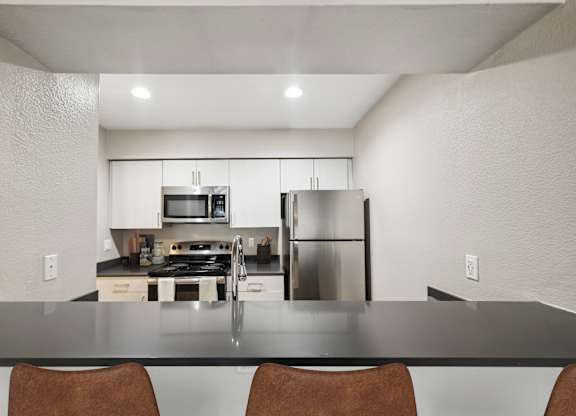 A modern kitchen with a black countertop and stainless steel appliances.