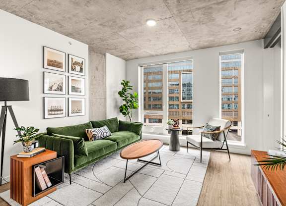 A living room with a green couch, a coffee table, and a large window with a view of a building.