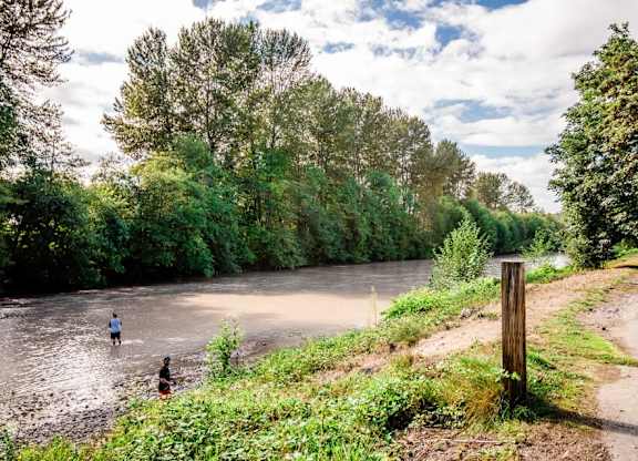 Two people are wading through a river in a natural landscape. at The Retreat, Sumner, Washington