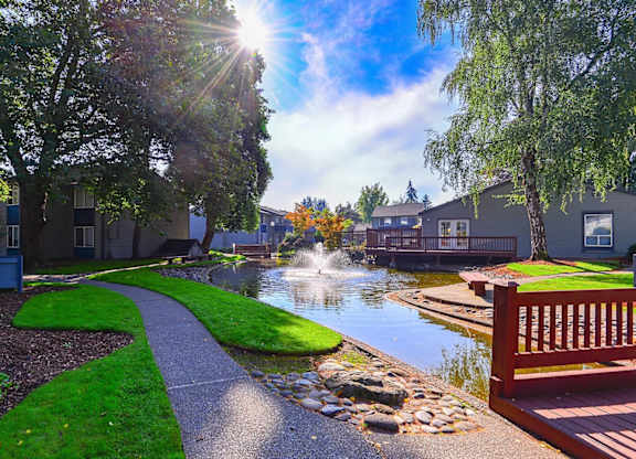 A sunny day in a residential area with a pond and a wooden bench. at The Lakes at Fife, Fife, WA, 98424