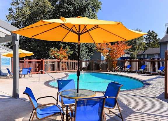 A yellow umbrella shades a table with blue chairs around a pool. at The Lakes at Fife, Fife, 98424