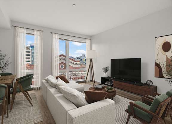 A living room with a white couch, a wooden coffee table, and a large window with a view of the city.