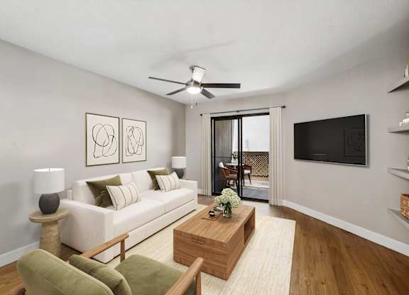 A living room with a white couch, a green chair, a wooden coffee table, and a flat screen TV mounted on the wall.