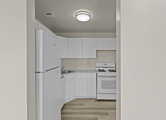 A white kitchen with a refrigerator, oven, and cabinets at Kensington House, Kensington, MD 20895
