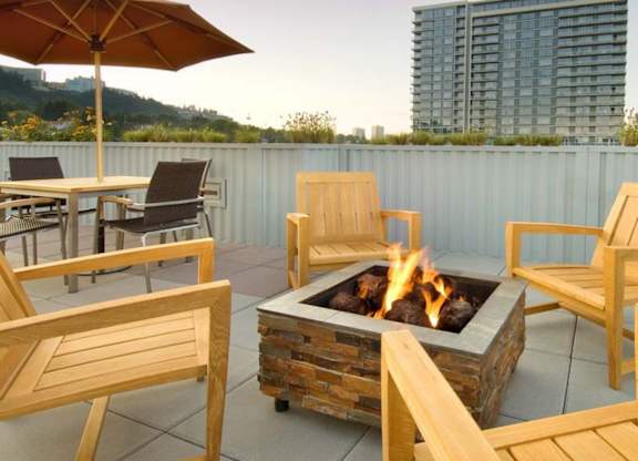 A fire pit on a patio surrounded by wooden chairs and an umbrella.