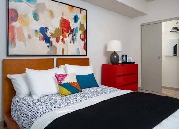 A bedroom with a large bed and a colorful painting above it.