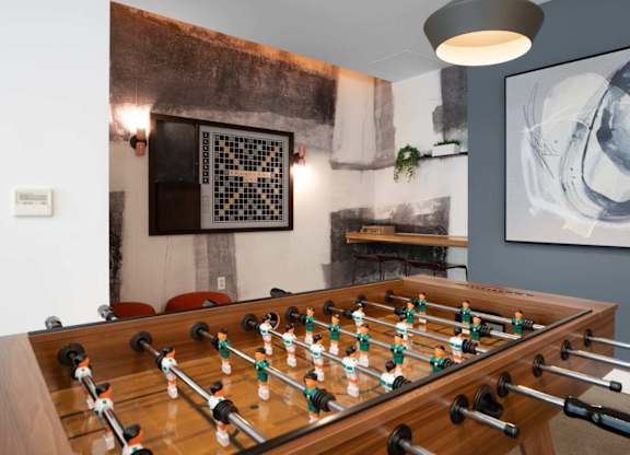 A foosball table is in the middle of a room with a grey wall and a black and white picture hanging above it.