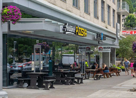 A street view of a pizzeria with people walking by.