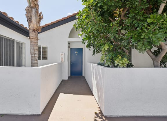 the entrance to a white house with a blue door and trees