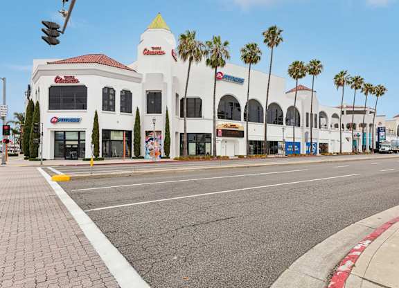 A white building with a red roof and palm trees in front.