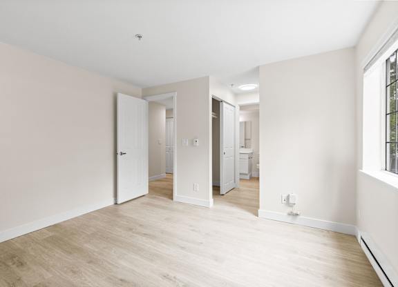 A room with white walls and wooden flooring with a doorway leading to another room.