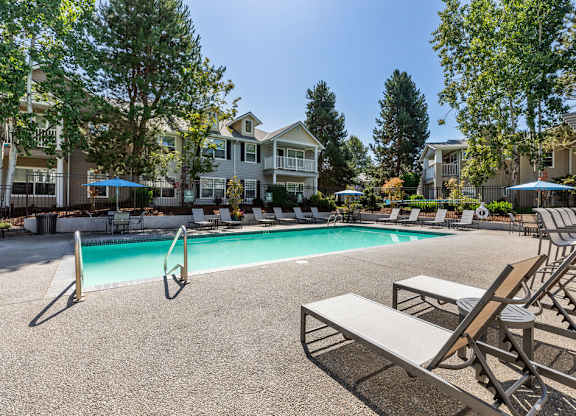 A pool surrounded by lounge chairs and trees.