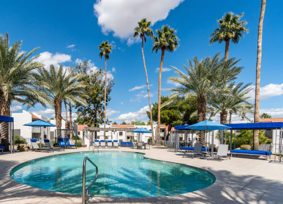 a swimming pool with blue umbrellas and palm trees in the background