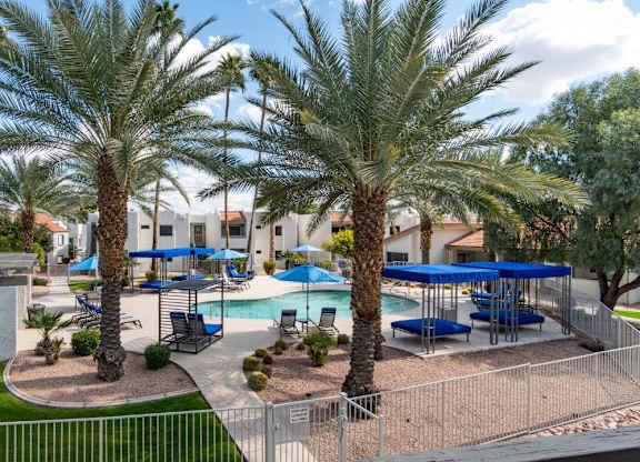 A pool surrounded by palm trees and blue umbrellas.