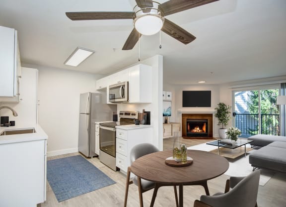 a kitchen and living room with a ceiling fan and a fire in the fireplace