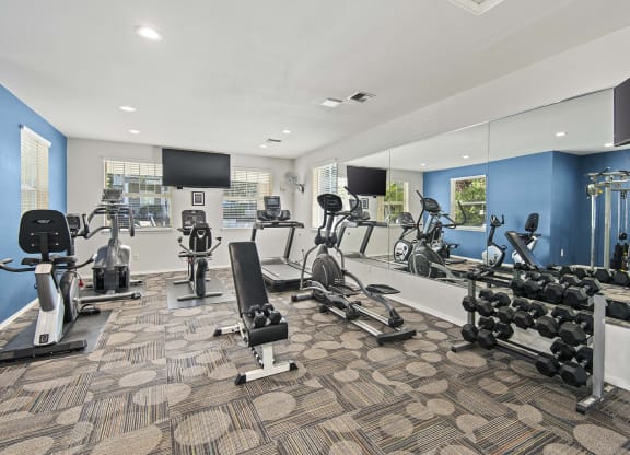 a gym with weights and cardio equipment in a room with mirrored walls