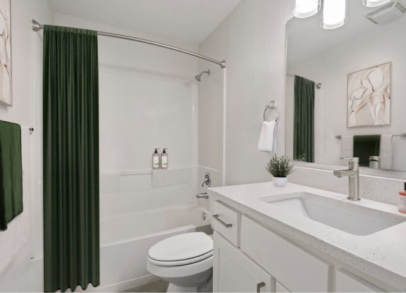 a white bathroom with a green shower curtain and a toilet and sink