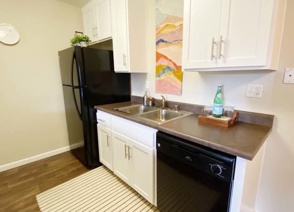 a small kitchen with white cabinets and a black refrigerator