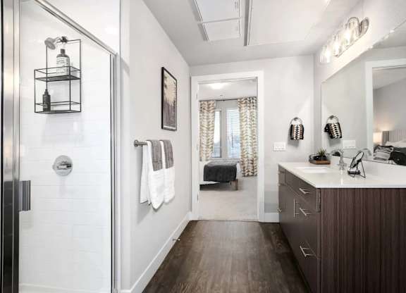 A bathroom with a white tile shower, a wooden vanity, and a large mirror.