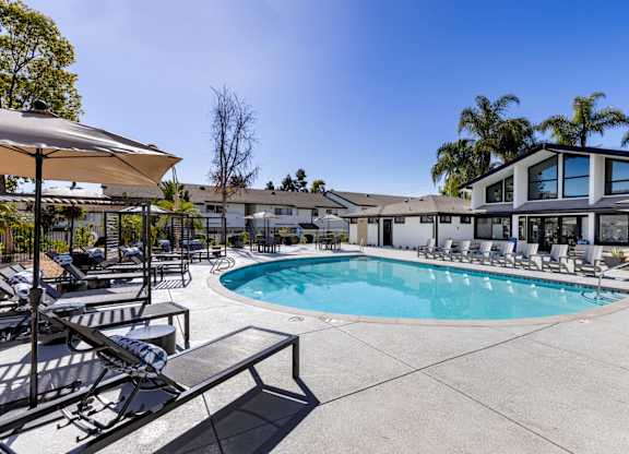 A pool area with sun loungers and a building in the background.