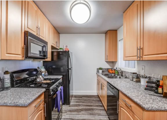 a kitchen with wood cabinets and granite counter tops and black appliances at Vista Promenade Apartments, Temecula, CA