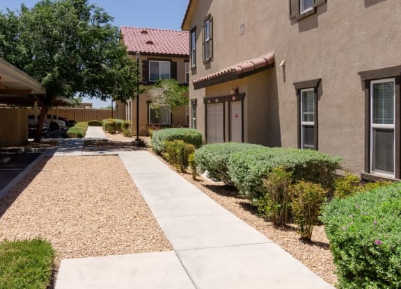 an exterior view of a building with a walkway and sidewalk at Riverton of the High Desert Apartments, Victorville, CA