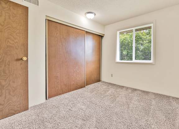 A room with a carpeted floor, a window, and a wooden door. at Winding Hills Apartments, Davenport
