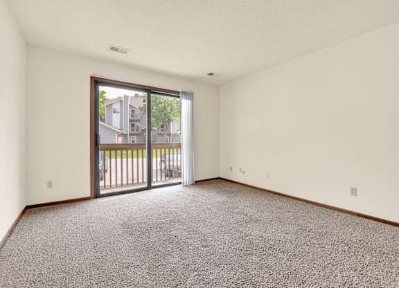 A room with a carpeted floor and a sliding glass door leading to a balcony.at Windsor Crest Apartments, Davenport