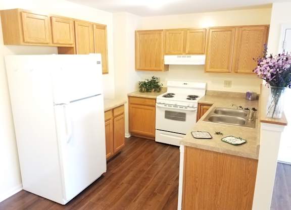 A white refrigerator stands in a kitchen with wooden cabinets and a stove.at Windsor Crest Apartments, Davenport 52807