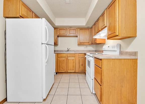 A white refrigerator stands in a kitchen with wooden cabinets and a white stove.at Windsor Crest Apartments, Davenport , Iowa