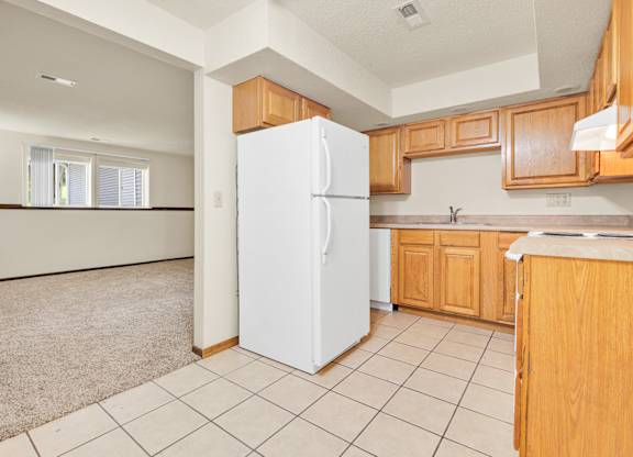 A kitchen with a white fridge and wooden cabinets.at Windsor Crest Apartments, Iowa