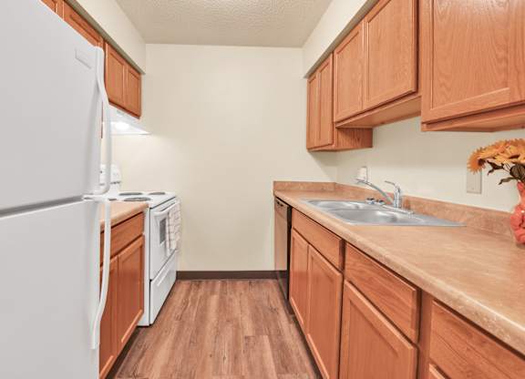 A kitchen with wooden cabinets and a white refrigerator. at Indian Ridge Apartments, Iowa