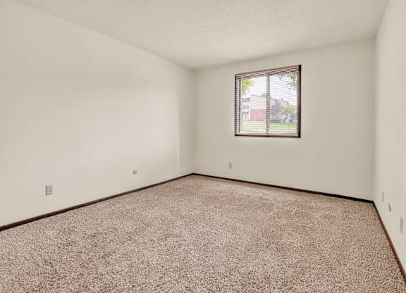 A room with a carpeted floor and a window. at Indian Ridge Apartments, Davenport, 52807