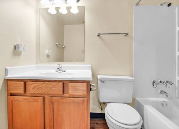 A white sink with a wooden cabinet and a white toilet in a bathroom. at Indian Ridge Apartments, Davenport, 52807
