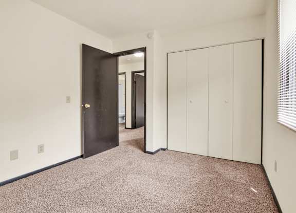 A room with a carpeted floor, a black door, and a white wardrobe. at Indian Ridge Apartments, Davenport, 52807