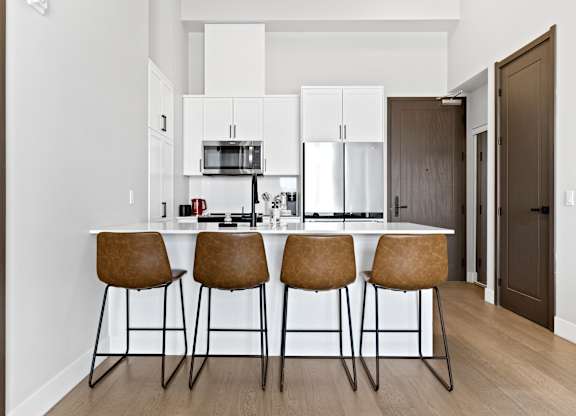 A kitchen with white cabinets and a bar area with brown chairs.